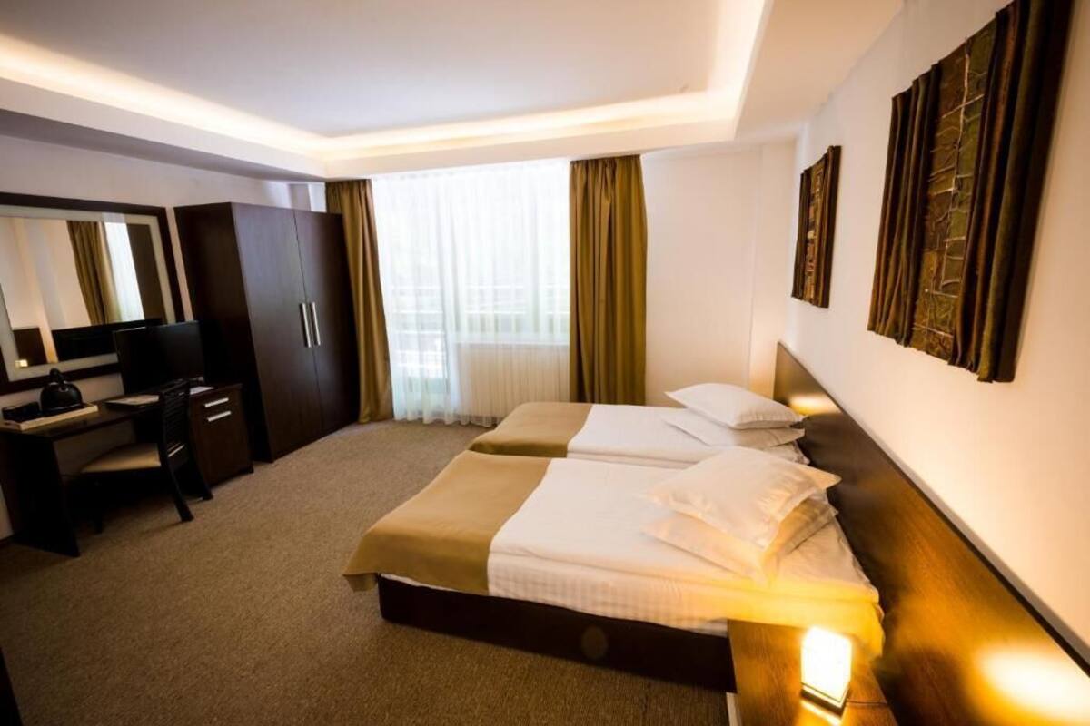 A hotel room with a bed, a desk, a chair, a wardrobe, and a large window with curtains.