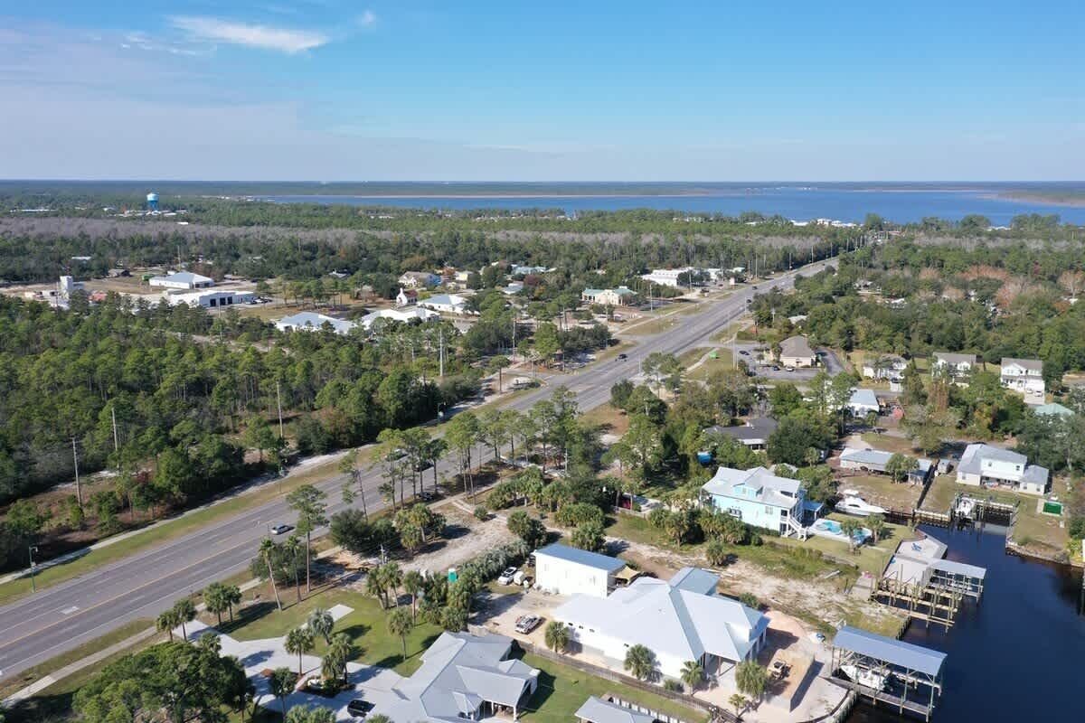 An aerial view of a residential area with houses, a road, and a body of water in the background.