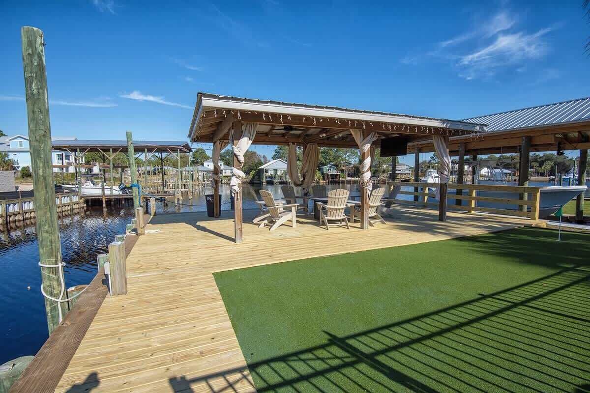 A wooden deck with a covered seating area and chairs, overlooking a body of water.