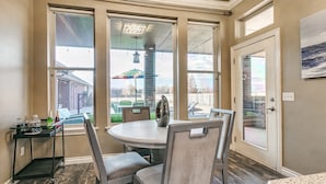 A dining area with a round table and four chairs, large windows, and a view of the outside.