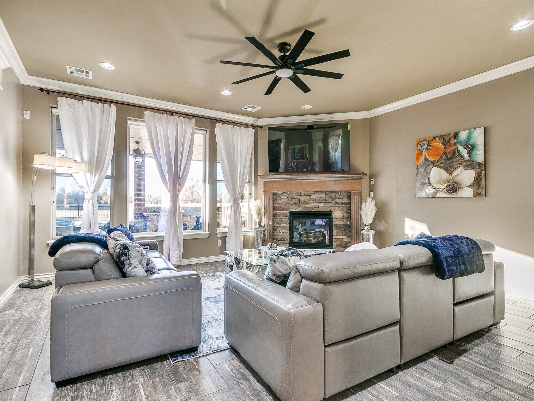 A modern living room with a fireplace, two sofas, a ceiling fan, and a large window with curtains.