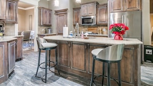 A modern kitchen with wooden cabinets, a stainless steel refrigerator, a microwave, and a large island with bar stools.