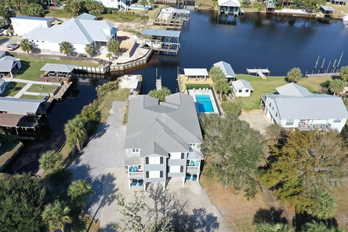 An aerial view of a residential area with a large house featuring a swimming pool, dock, and surrounding greenery.