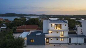 Een modern, meerlaags gebouw met een plat dak, grote ramen en een uitzicht op een meer en heuvels op de achtergrond.