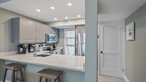 Una cocina moderna con armarios blancos, electrodomésticos de acero inoxidable, encimera de mármol y una puerta con detalles decorativos.
