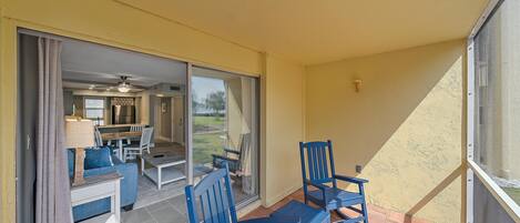 A patio with blue chairs and a table, a sliding glass door leading to a kitchen and dining area, and a yellow exterior wall.