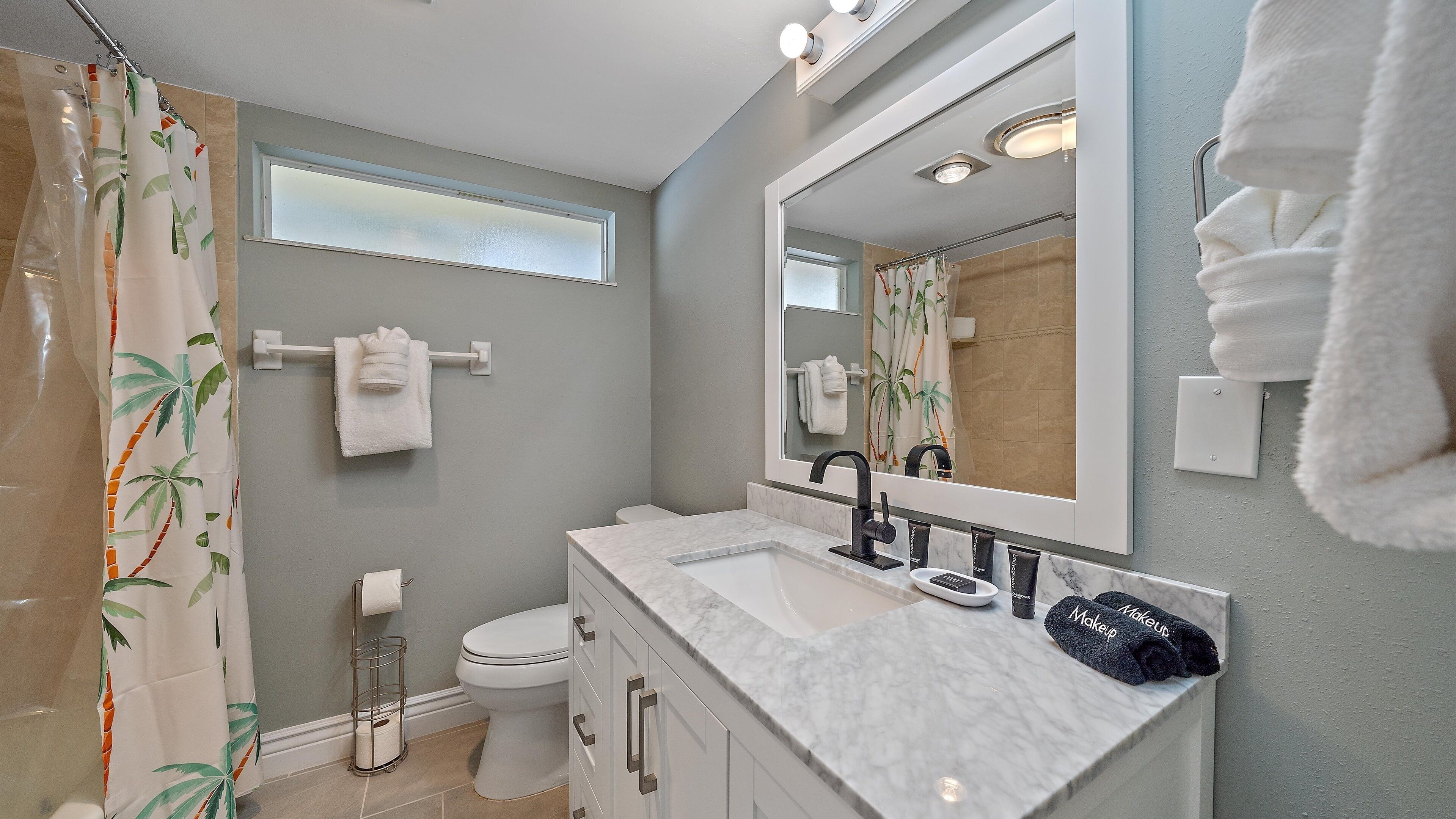 Une salle de bain avec un rideau de douche, des toilettes, un lavabo avec un miroir et des serviettes sur un porte-serviettes.