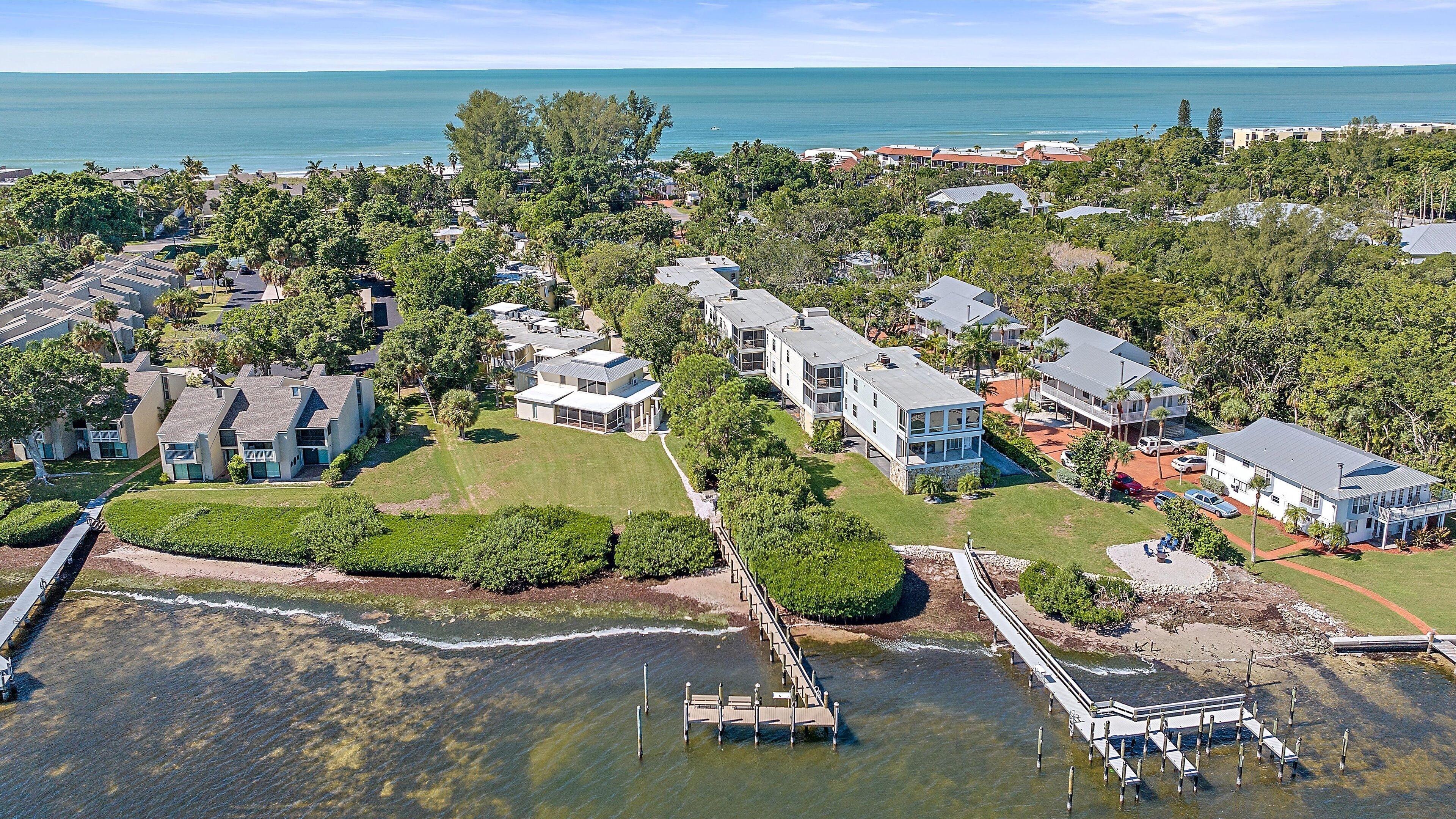 Vue aérienne d’une zone résidentielle côtière, avec des maisons, une jetée et une plage.