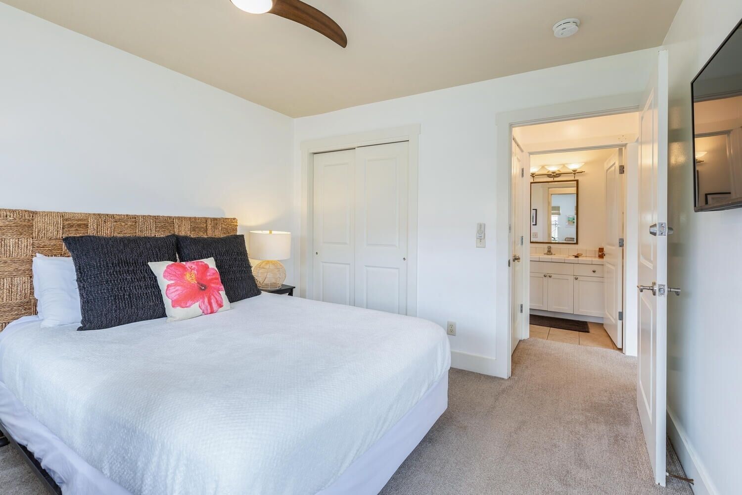 A bedroom with a large bed, a wooden headboard, a nightstand with a lamp, and a door leading to a bathroom.