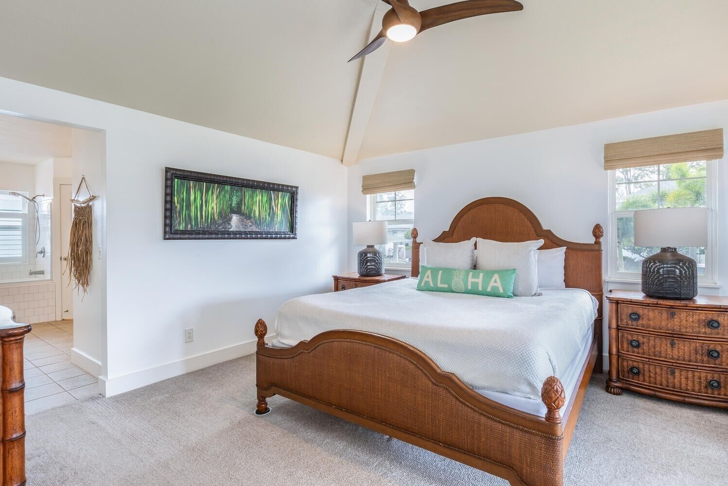 A spacious bedroom with a large bed, a ceiling fan, a window with a view, and a wall-mounted artwork.