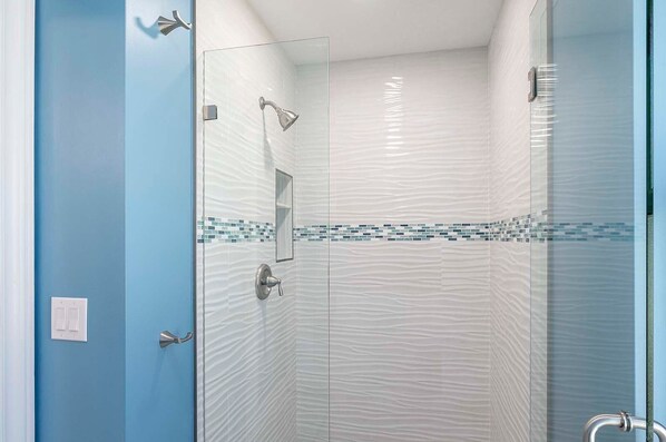 Ducha con paredes de vidrio, pared texturizada y puerta azul.