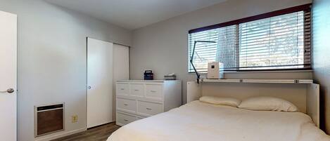 Un dormitorio con cama, cómoda, radiador y ventana con persianas.
