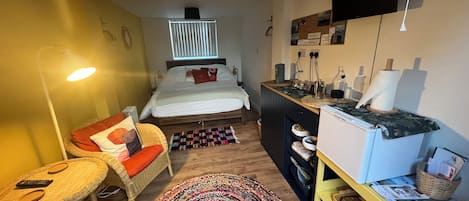 A compact hotel room with a bed, a desk, a chair, a lamp, and a TV.