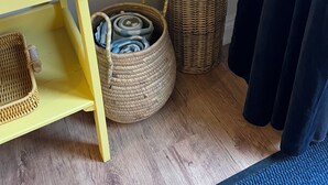 Esquina de una habitación con una mesa amarilla, cestas de mimbre y un tapete azul.