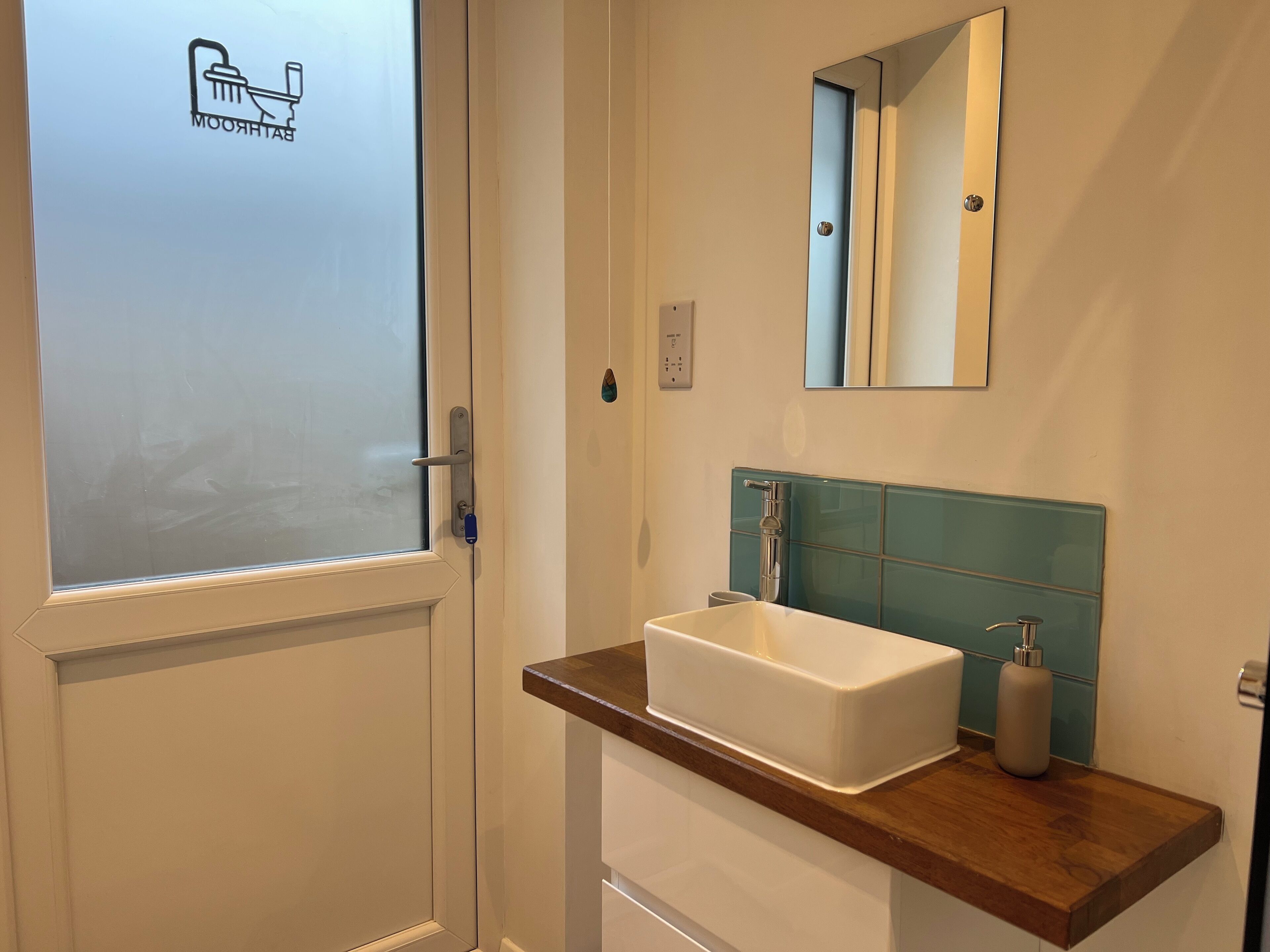 Une salle de bain avec un lavabo blanc, un miroir et une porte en verre dépoli.