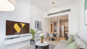 Een moderne woonkamer met een flatscreen televisie, een eethoek met een ronde tafel en een keuken met een koelkast.