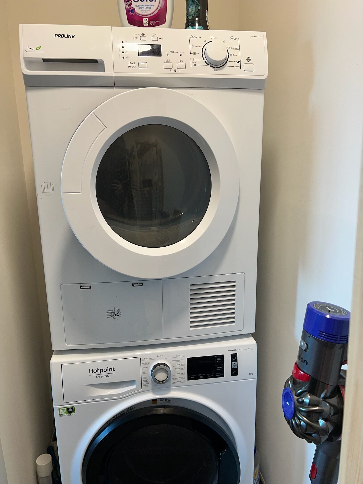 Een gestapelde wasmachine en droger met bedieningspaneel, een digitaal display en een waterfilterfles.