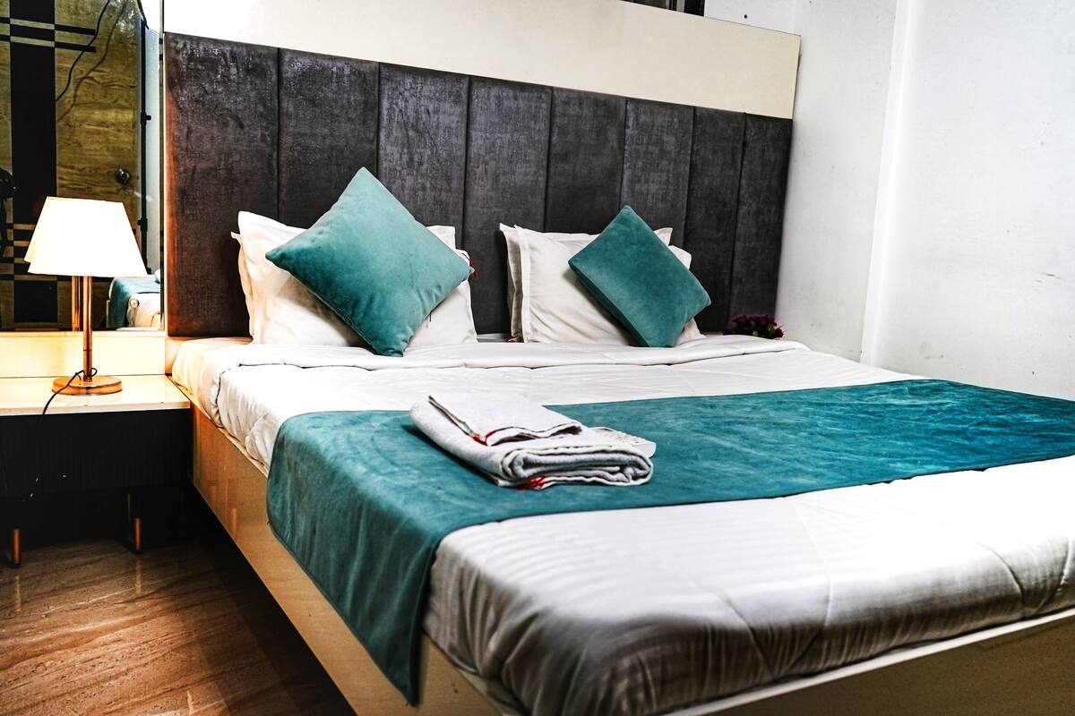 Cama bem arrumada com colcha verde-água, duas almofadas verde-água e uma toalha branca dobrada.