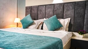 Un letto rifatto con una coperta color petrolio e cuscini, una lampada da comodino e una piccola pianta in vaso su un tavolino.