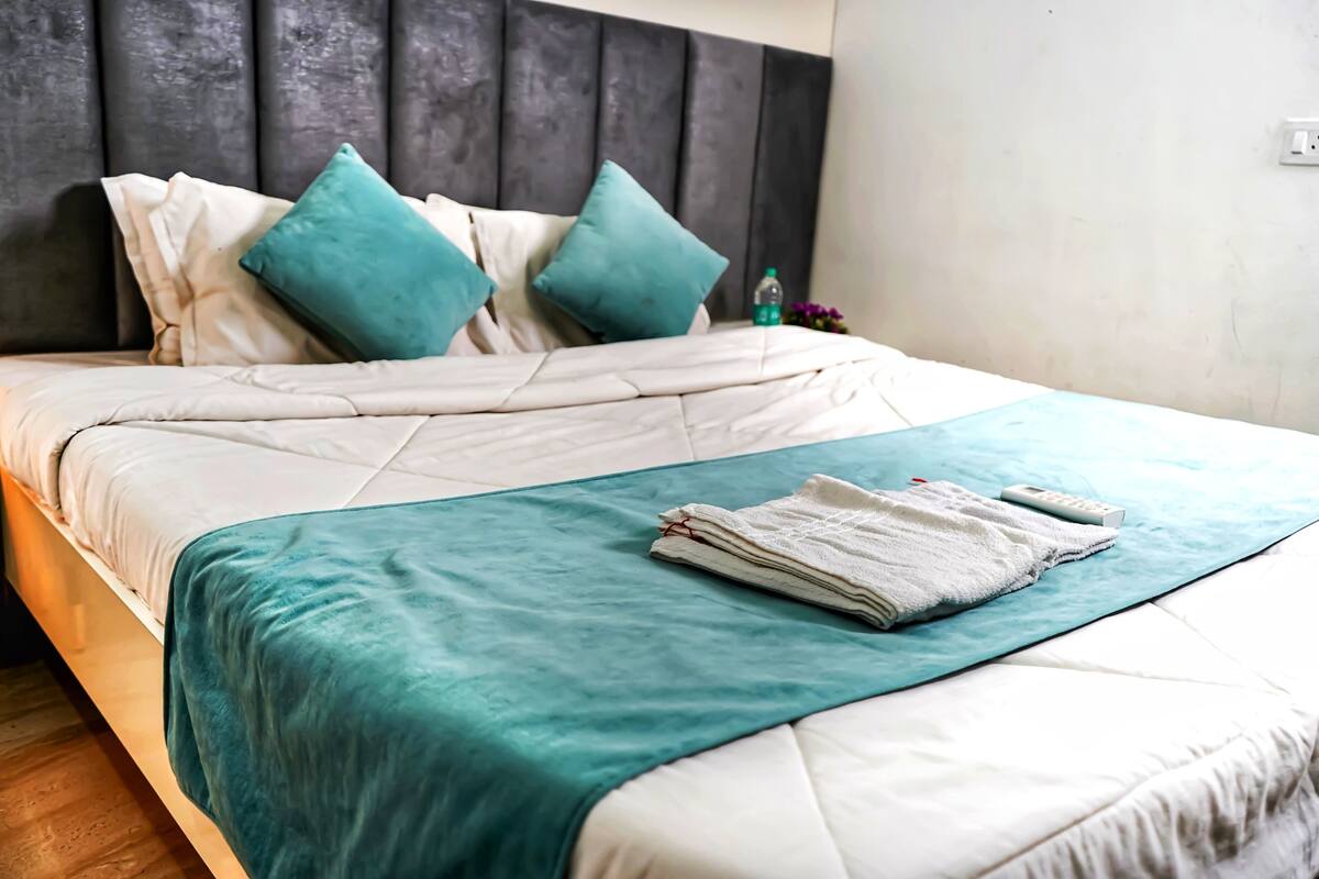 Uma cama bem arrumada com um cobertor verde-água e roupa de cama branca, uma cabeceira cinza e uma pequena garrafa de água na mesa de cabeceira.
