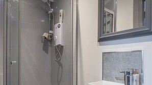 Une salle de bain moderne avec une douche à parois de verre, un meuble-lavabo blanc avec un miroir et un mur recouvert de carreaux.