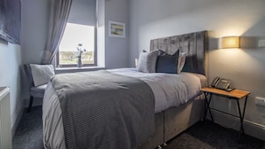 Une chambre à coucher avec un lit, une chaise, une table de chevet avec une lampe et une fenêtre avec des rideaux.