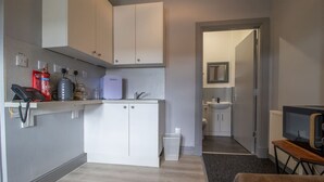 Cocina compacta con armarios blancos, cafetera y microondas.