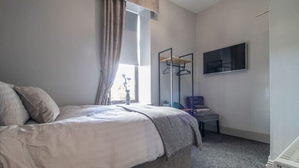 Un dormitorio con cama, televisor, espejo y silla.