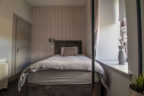 A bedroom with a bed, a bedside table, a window with a view, and a radiator.