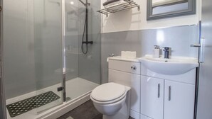 Un baño moderno con ducha acristalada, inodoro blanco, lavabo con espejo y toallero.