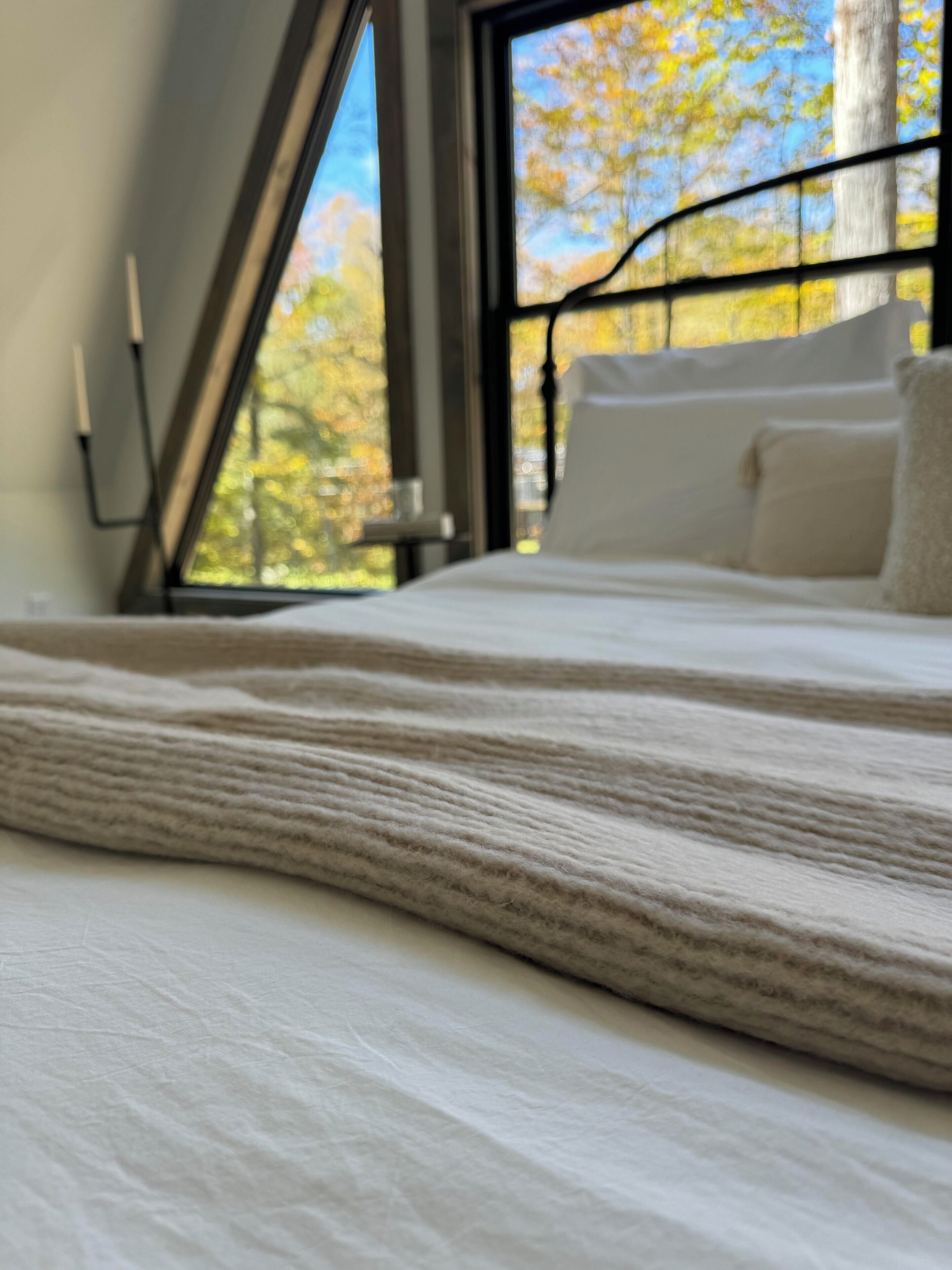 A bed with a textured blanket, a window with a view of trees, and a metal headboard.