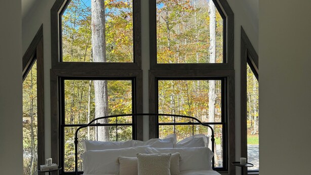 A bedroom with a large bed, multiple windows, and a view of trees. - Pocono Lakefront A-Frame Cabin (Pocono Lake)