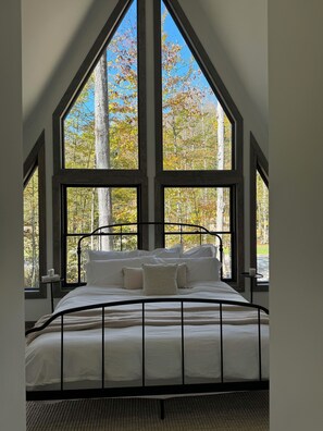 Un dormitorio con una cama grande, varias ventanas y vistas a árboles.