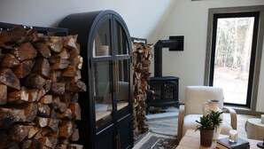 A cozy living room with a fireplace, a large wooden log wall, a comfortable chair, and a coffee table with a plant and books. - Pocono Lakefront A-Frame Cabin (Pocono Lake)
