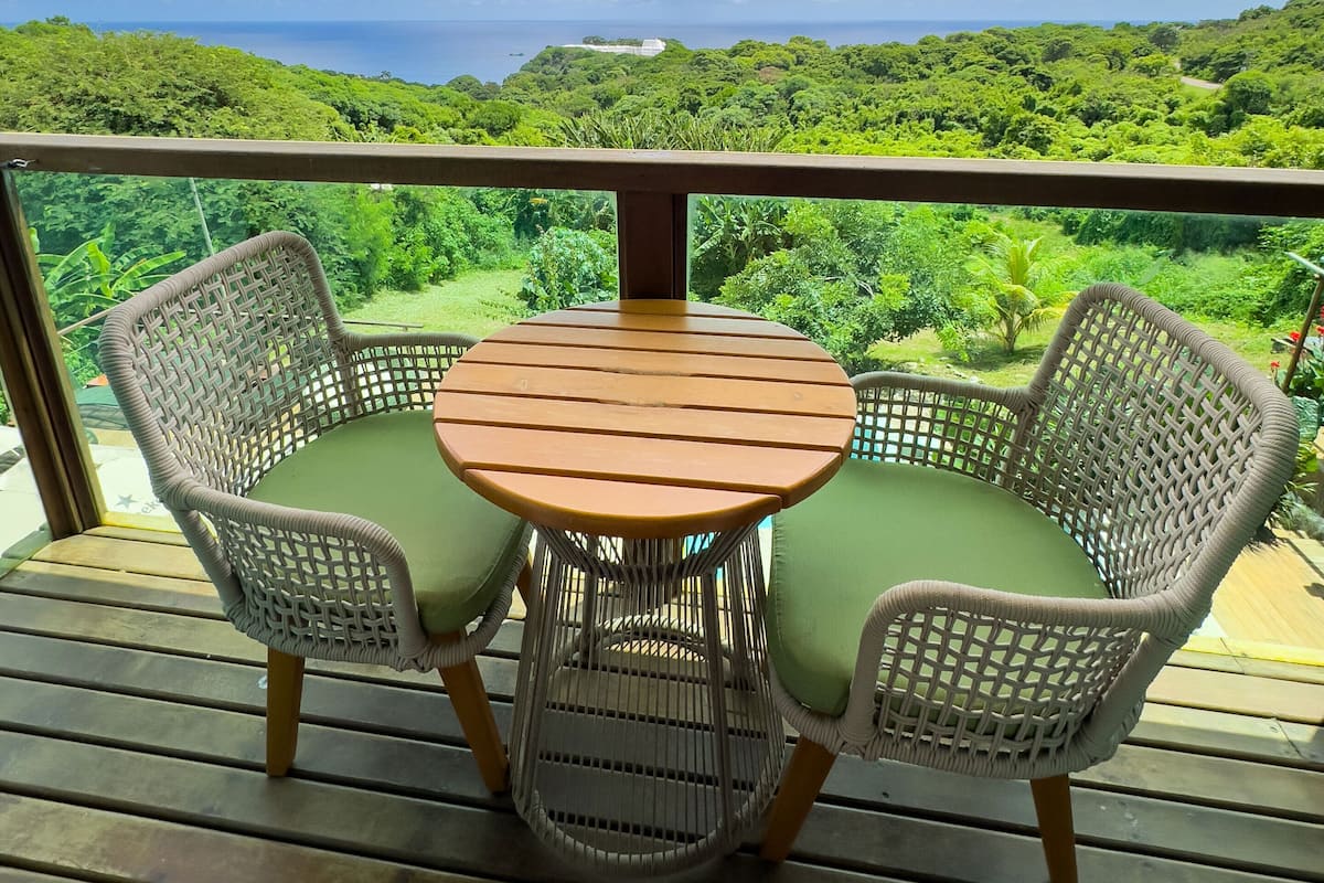 Uma mesa de madeira redonda com duas cadeiras de vime, cada uma com uma almofada verde, sobre um deck de madeira.