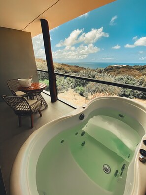 Un balcon avec un jacuzzi, une table avec un seau et un verre, et une vue sur un paysage désertique.