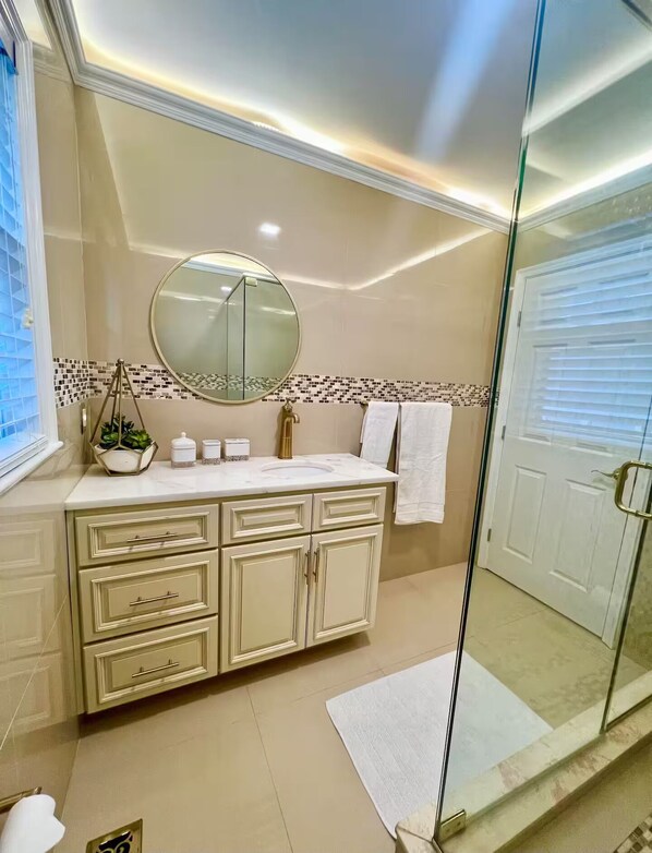 A modern bathroom with a vanity, a round mirror, and a glass shower enclosure.