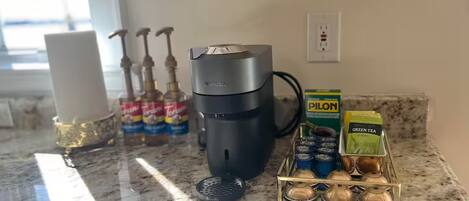 A kitchen counter with a coffee maker, a kettle, and a coffee pod holder.