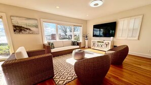 A spacious living room with a large window, a flat-screen TV, wicker furniture, and a patterned rug. - Waterview Oasis by Buckroe Beach (Hampton)