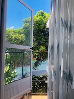 Ventana abierta con vistas a vegetación exuberante y cielo azul despejado.