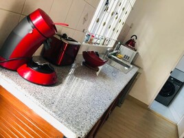 Una cocina con un electrodoméstico rojo, un lavabo, una tetera y una lavadora.