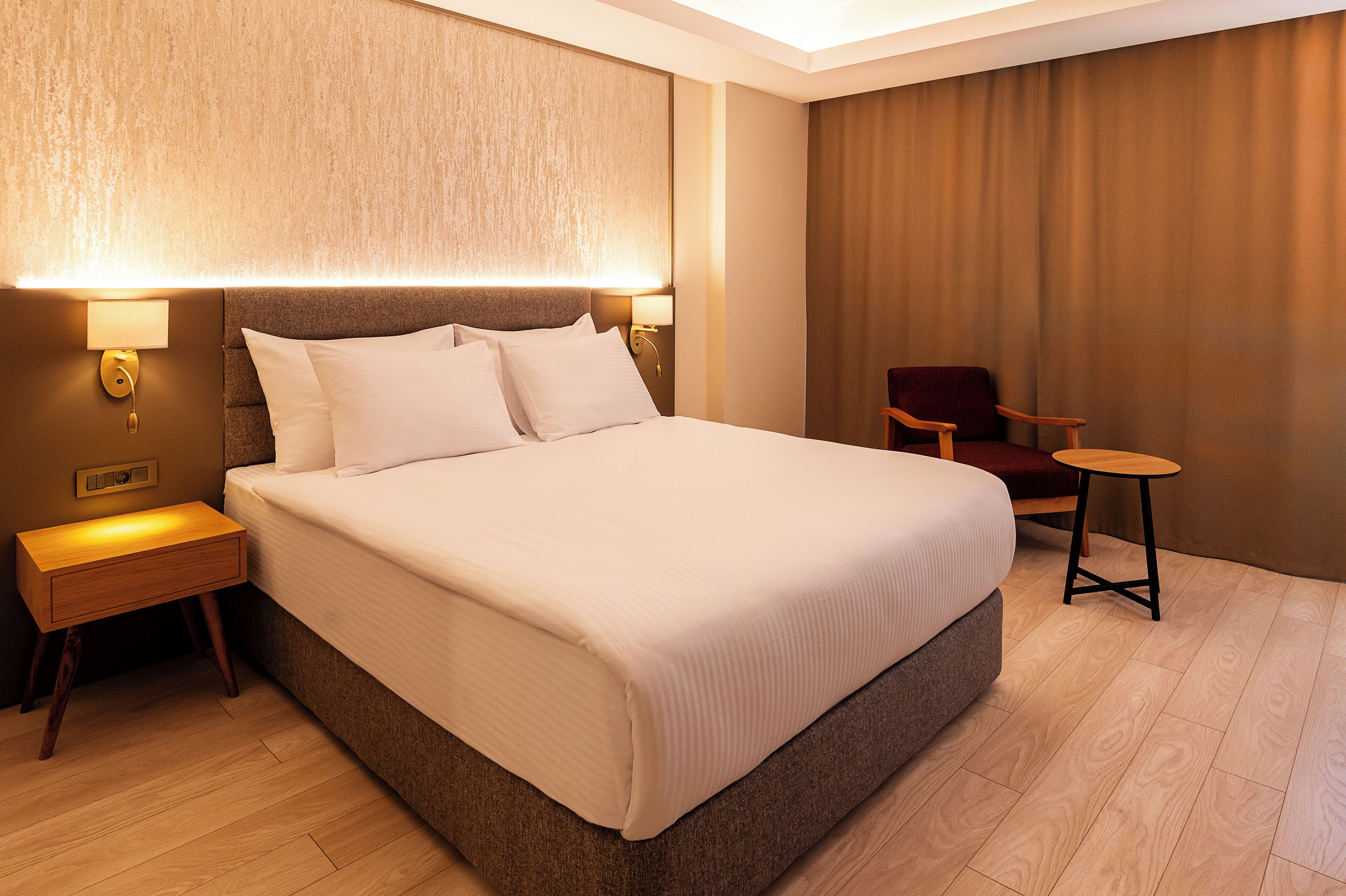 A hotel room with a large bed, a nightstand, a chair, and a wall-mounted lamp.