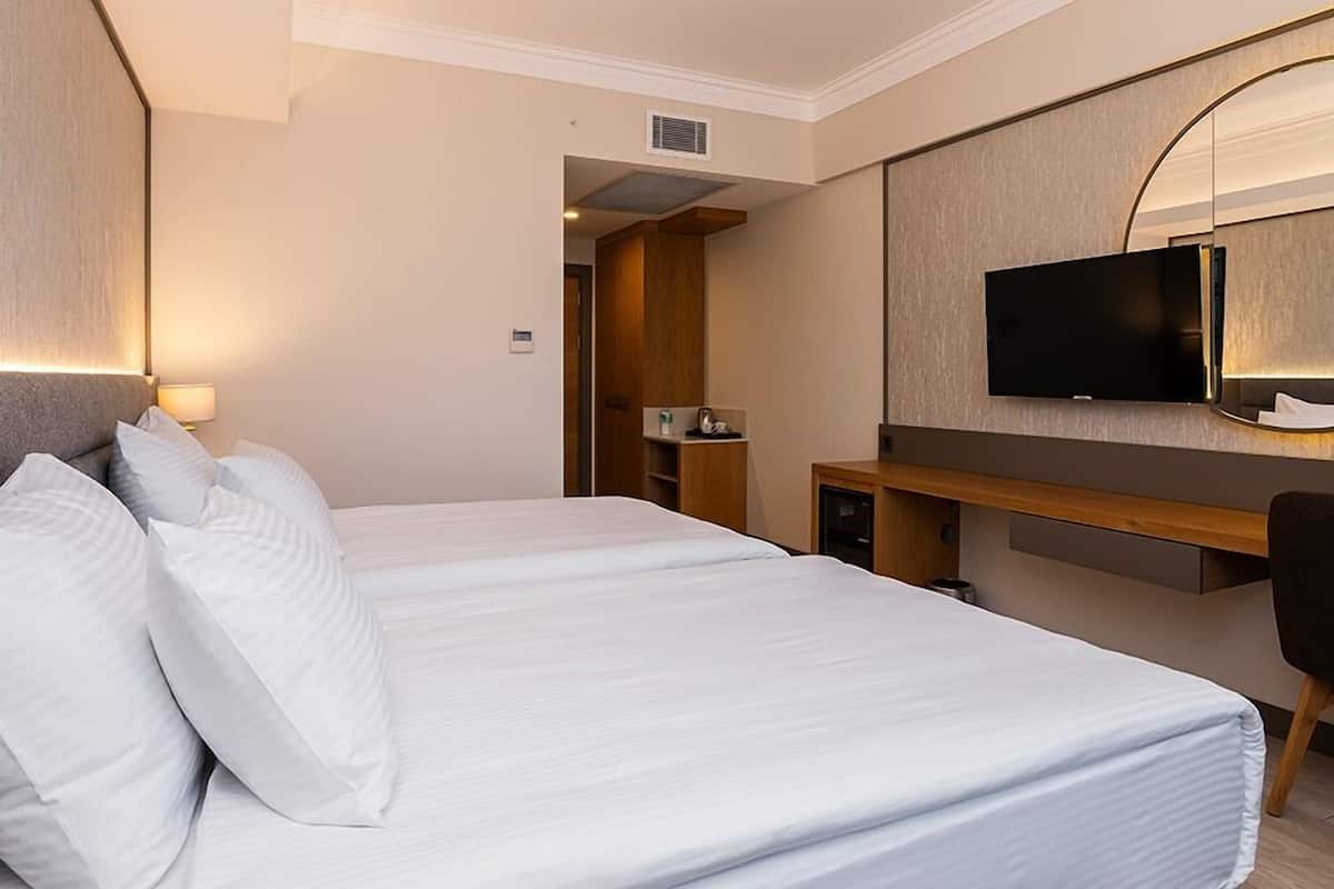 Una habitación de hotel con una cama grande, un escritorio, un televisor y un espejo.