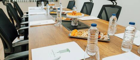Un salón de conferencias con una larga mesa, sillas negras, botellas de agua y una pizarra con un logotipo.