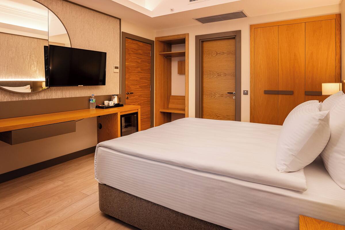 Habitación de hotel con cama, televisor, armario de madera y espejo.