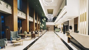 Een ruime lobby met een marmeren vloer, een zithoek met banken en fauteuils, een receptiebalie en een moderne kroonluchter.