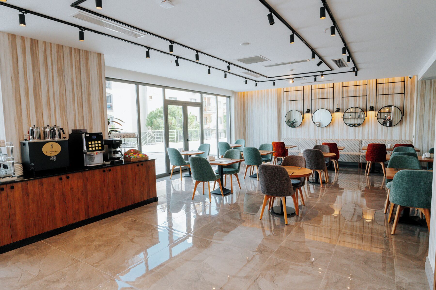 A modern cafe with a wooden counter, espresso machines, and seating area with chairs and tables.