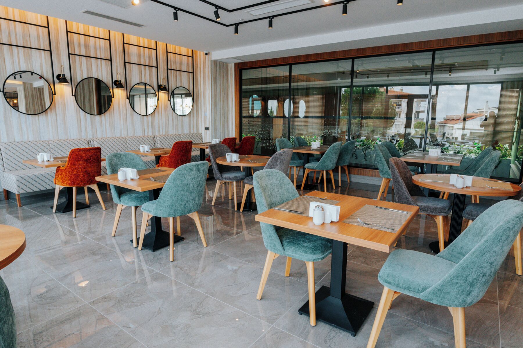 A modern cafe with round tables, teal chairs, and a wooden wall with mirrors.
