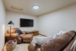 Un soggiorno con televisione a schermo piatto, divani in pelle, un tavolino in legno e una lampada da terra.