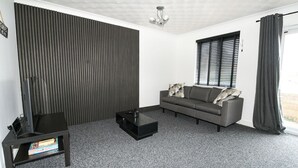 Una sala de estar moderna con un sofá gris, una mesa de centro negra y un televisor sobre un mueble.